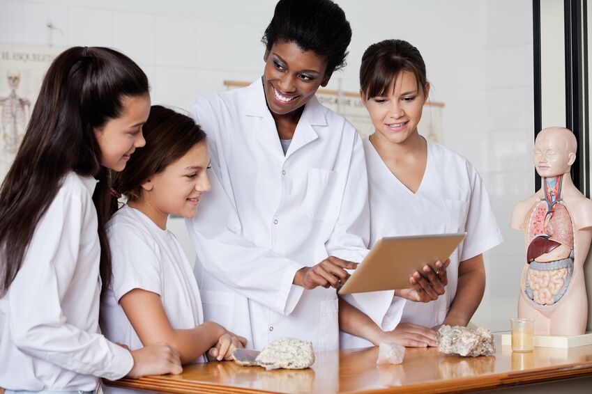 Teacher Looking At Schoolgirls While Using Tablet In Biology Cla